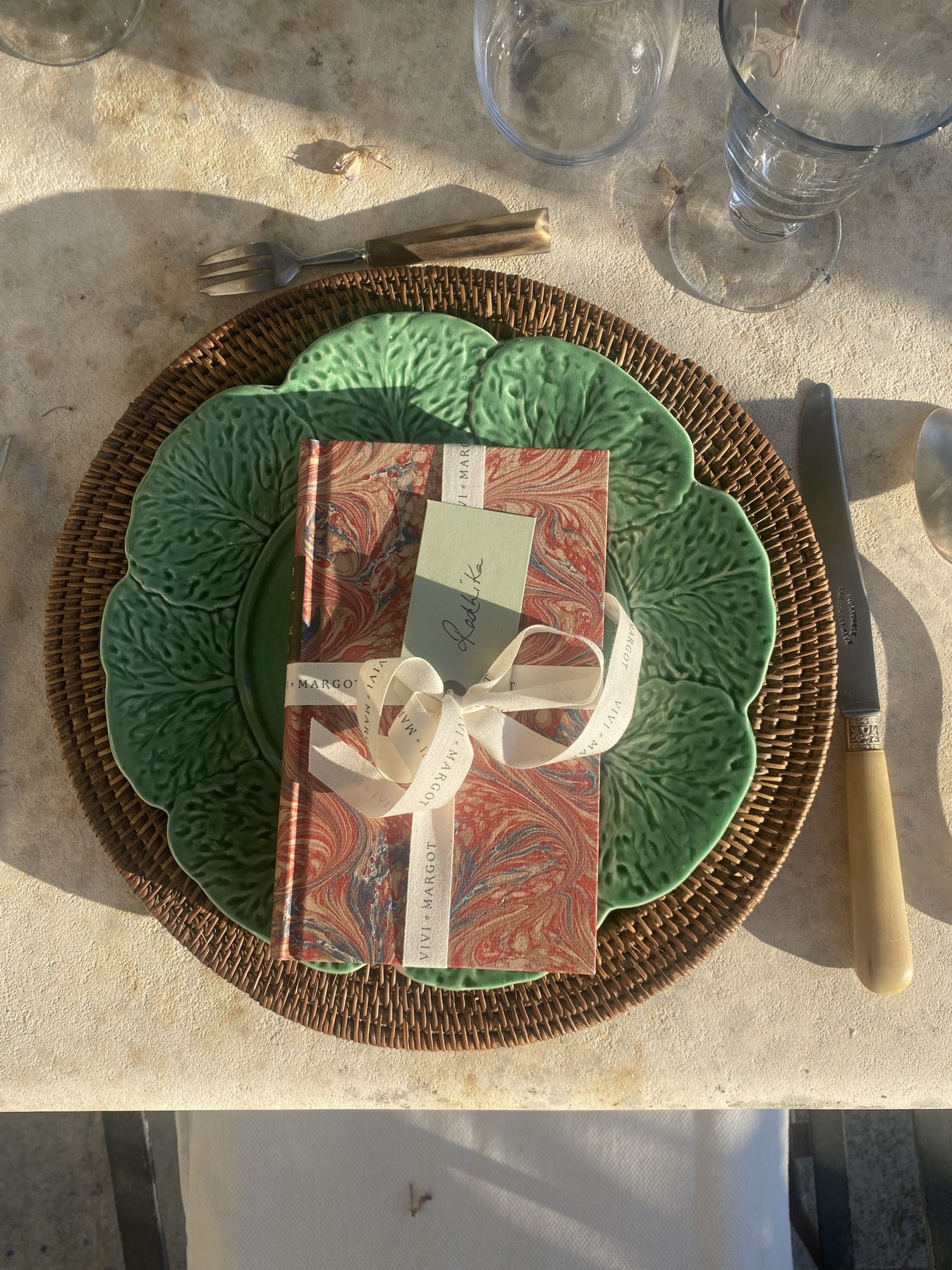 Détail du couvert — assiette verte en céramique sur set en rotin et menu de table